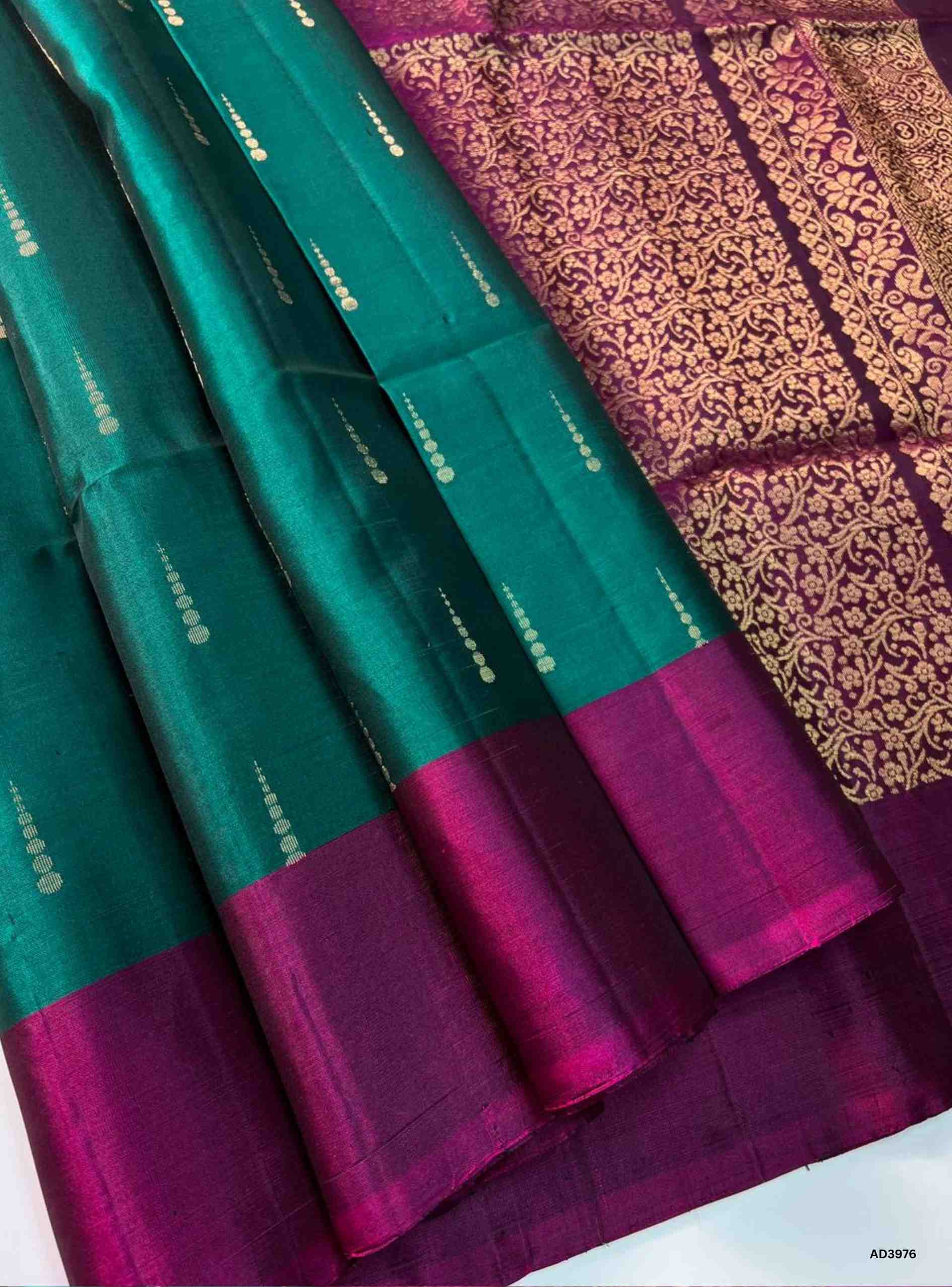 The Emerald Green & Pink Bhutta Soft Silk Saree is a radiant handwoven creation that celebrates festive grandeur with a jewel‑tone palette. The lush emerald green shade radiates prosperity and cultural richness, while the pink tone adds feminine charm and celebratory brilliance. The bhutta weave, adorned with intricate motifs, enhances the saree’s artistry, while zari highlights on the border and pallu lend a shimmering appeal. Perfect for weddings, temple ceremonies, and cultural gatherings, this saree emb