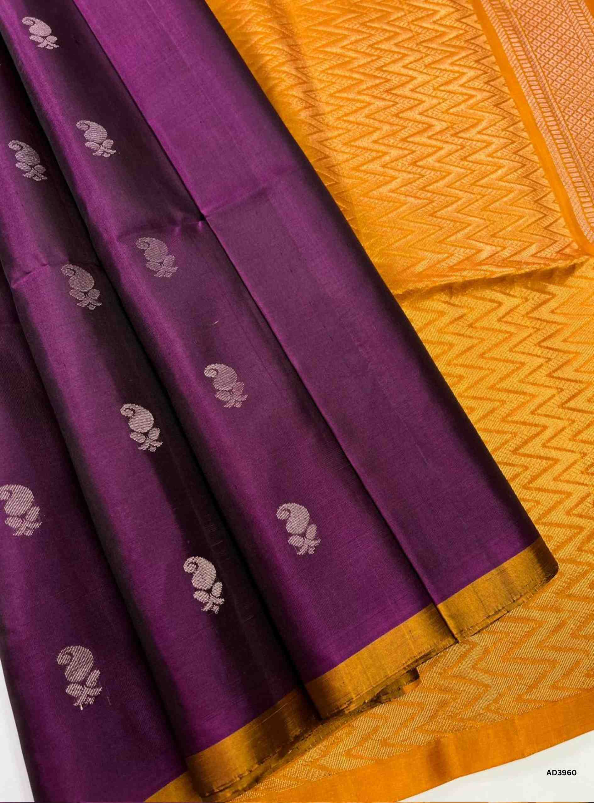 The Burgundy & Mango Yellow Bhutta Soft Silk Saree is a vibrant handwoven creation that celebrates festive grandeur in dual tones. The deep burgundy shade radiates regal elegance, while the mango yellow adds auspicious brilliance and warmth. The bhutta weave, adorned with delicate motifs, enhances the saree’s charm, while zari highlights on the border and pallu lend a shimmering appeal. Perfect for weddings, temple ceremonies, and cultural gatherings, this saree embodies South Indian weaving tradition with