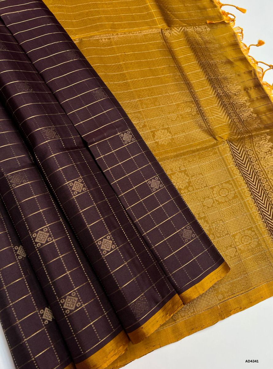 The Coffee Brown & Brown Checkered Soft Silk Saree is a timeless handwoven creation that radiates cultural richness and understated elegance. The coffee brown shade conveys warmth, devotion, and heritage charm, while the brown checks add subtle depth and classic appeal. Enhanced with pure gold zari borders and a lustrous drape, this saree is perfect for weddings, temple ceremonies, and festive occasions. A versatile masterpiece, it blends earthy tones with checkered artistry in South Indian weaving traditio