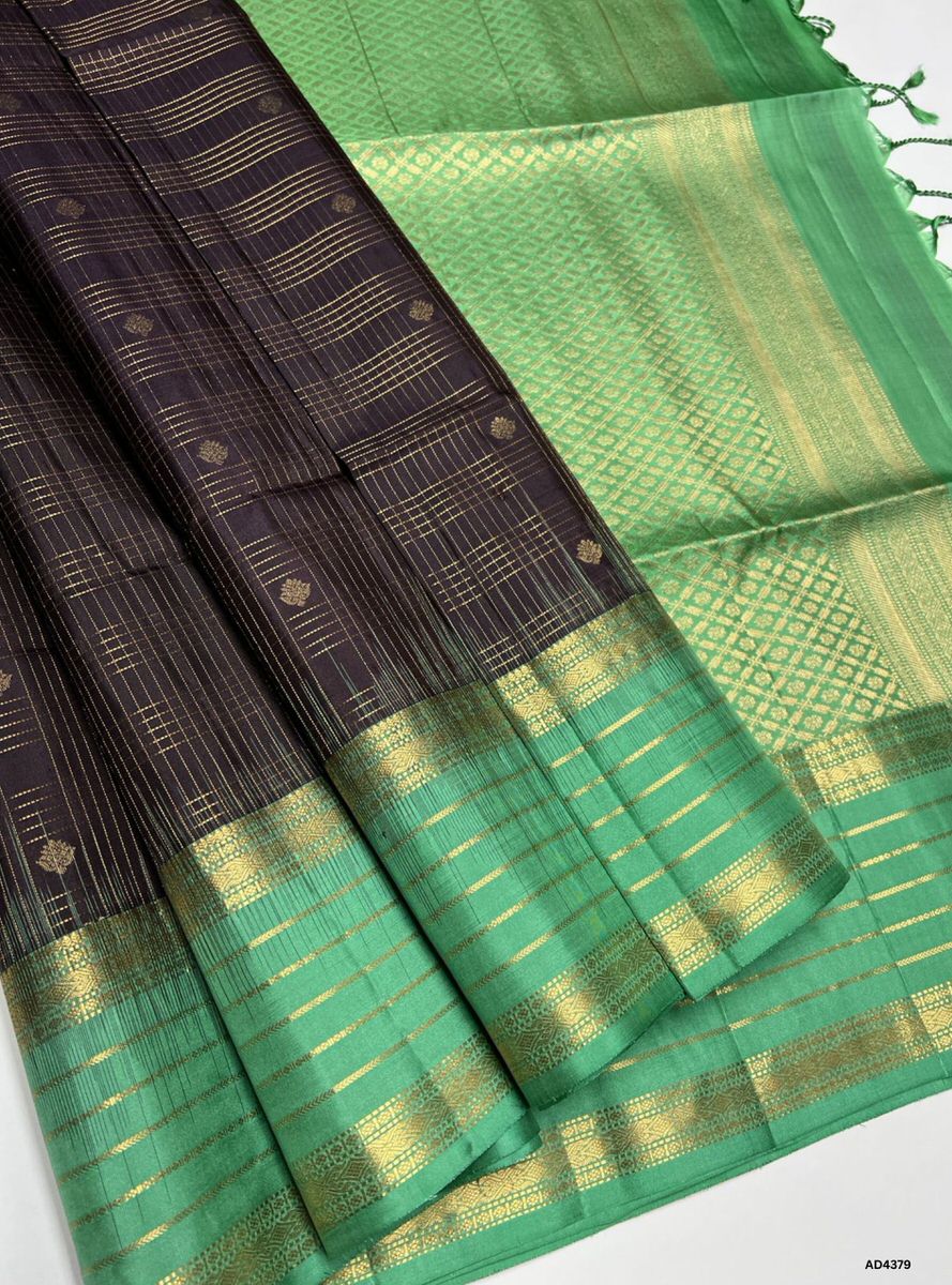 The Coffee Brown & Mint Green Checkered Retta Pet Soft Silk Saree is a refined handwoven creation that radiates cultural richness and festive charm. The coffee brown shade conveys devotion, warmth, and heritage depth, while the mint green checks add freshness, vibrance, and celebratory brilliance. Enhanced with pure gold zari borders and a lustrous drape, this saree is perfect for weddings, temple ceremonies, and festive occasions. A timeless masterpiece, it blends earthy richness with pastel vibrance in th