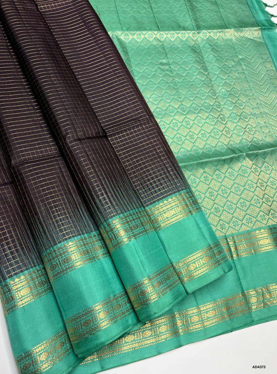 The Coffee Brown & Mint Green Checkered Retta Pet Soft Silk Saree is a refined handwoven creation that radiates cultural richness and festive charm. The coffee brown shade conveys devotion, warmth, and heritage depth, while the mint green checks add freshness, vibrance, and celebratory brilliance. Enhanced with pure gold zari borders and a lustrous drape, this saree is perfect for weddings, temple ceremonies, and festive occasions. A timeless masterpiece, it blends earthy richness with pastel vibrance in th