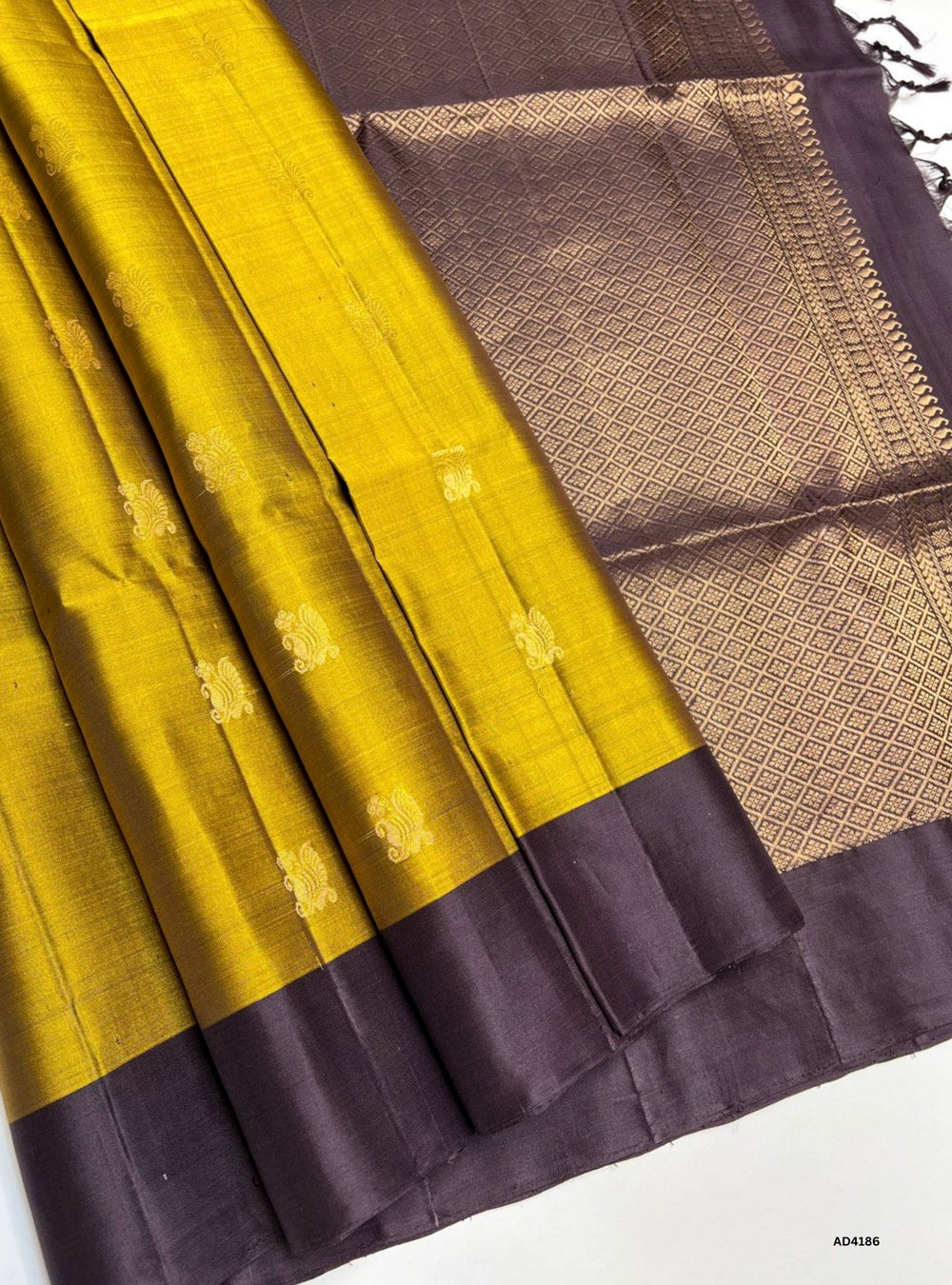 The Fenugreek & Coffee Brown Soft Silk Saree is a heritage handwoven creation that radiates earthy elegance and cultural grandeur. The fenugreek shade conveys warmth, prosperity, and festive charm, while the coffee brown adds depth, stability, and timeless sophistication. Enhanced with pure gold zari borders and a lustrous drape, this saree is perfect for weddings, temple ceremonies, and cultural gatherings. A timeless piece of artistry, it blends natural tones with the grandeur of South Indian weaving trad