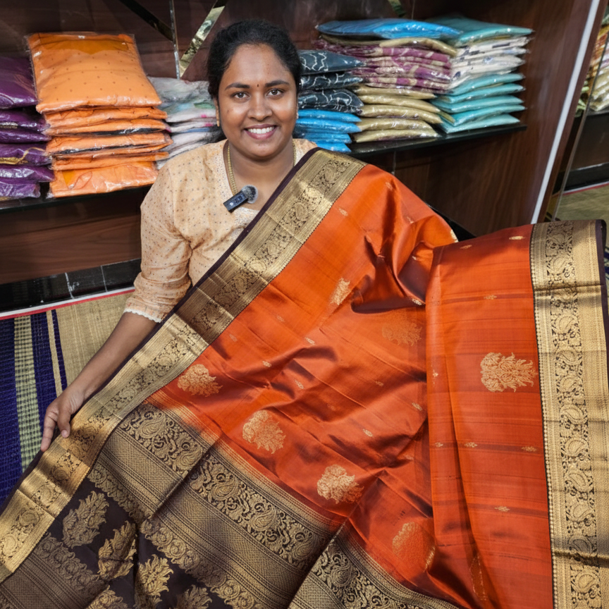 Woman wearing an orange saree with a gold border in a store setting.
