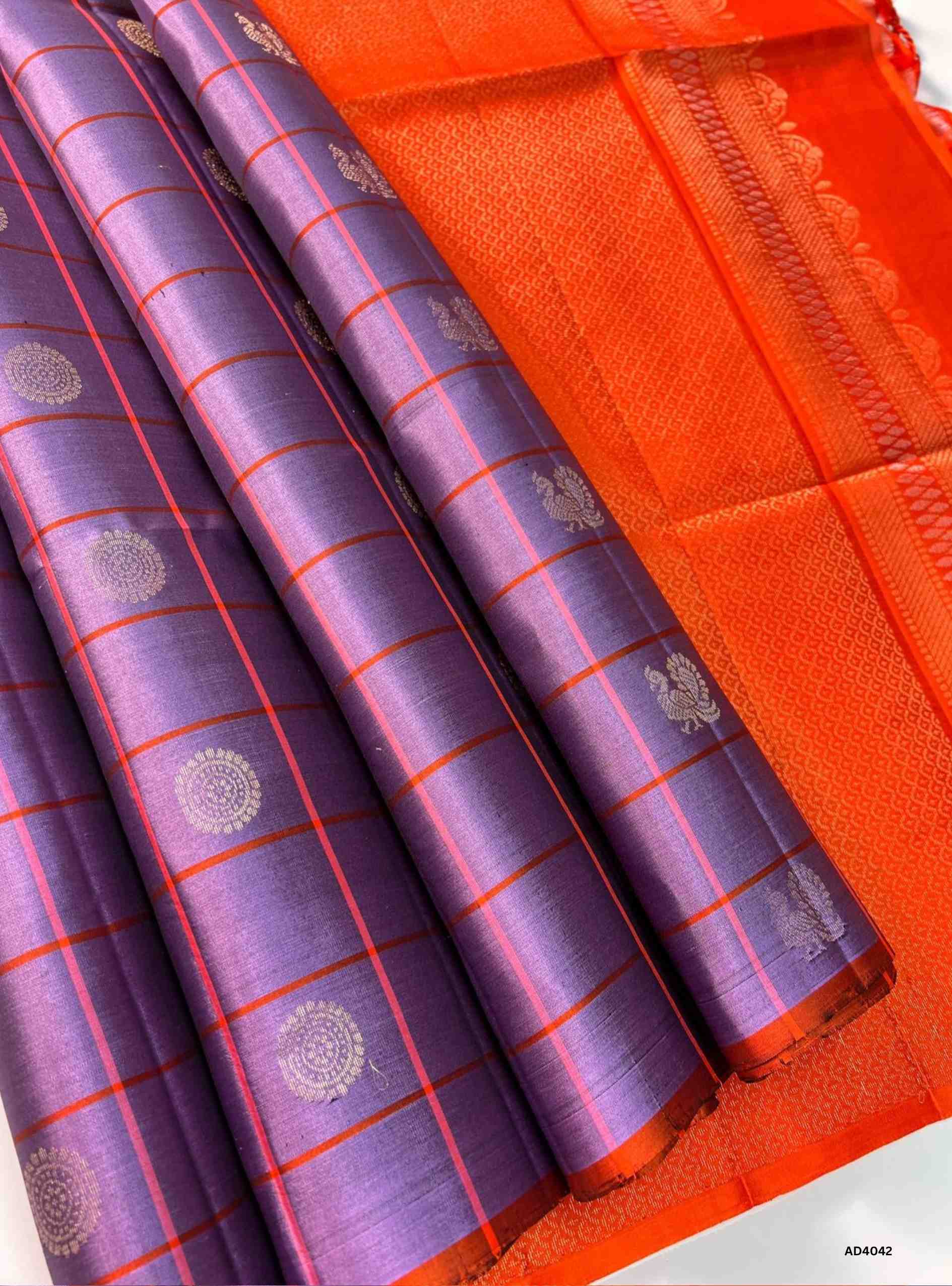 The Grape & Orange Checkered Soft Silk Saree is a radiant handwoven creation that celebrates festive brilliance and cultural artistry. The regal grape shade symbolizes prosperity and elegance, while the vibrant orange adds auspicious warmth and celebratory charm. The checkered weave, enriched with delicate motifs, creates a rhythmic visual appeal, while zari highlights on the border and pallu lend a shimmering finish. Perfect for weddings, temple ceremonies, and cultural gatherings, this saree embodies Sout