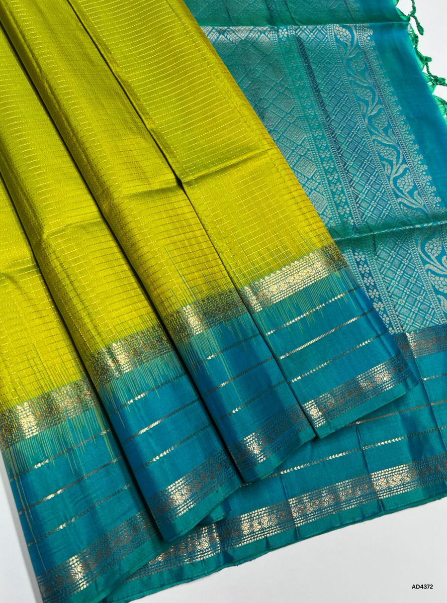 The Lime Yellow & Rama Blue Checkered Retta Pet Soft Silk Saree is a radiant handwoven creation that embodies festive charm and cultural richness. The lime yellow shade conveys joy, prosperity, and celebratory brilliance, while the Rama blue checks symbolize auspiciousness, devotion, and timeless elegance. Enhanced with pure gold zari borders and a lustrous drape, this saree is perfect for weddings, temple ceremonies, and festive occasions. A timeless masterpiece, it blends vibrant brightness with heritage