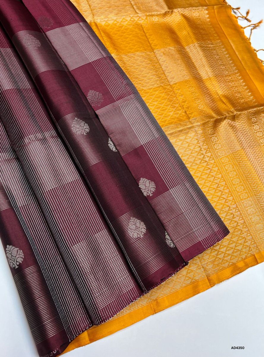 The Maroon & Mustard Yellow Checkered Soft Silk Saree is a majestic handwoven creation that radiates festive brilliance and cultural richness. The maroon shade symbolizes devotion, prosperity, and heritage depth, while the mustard yellow checks add vibrance, auspiciousness, and celebratory warmth. Enhanced with pure gold zari borders and a lustrous drape, this saree is perfect for weddings, temple ceremonies, and festive occasions. A timeless masterpiece, it blends jewel‑tone grandeur with checkered artistr