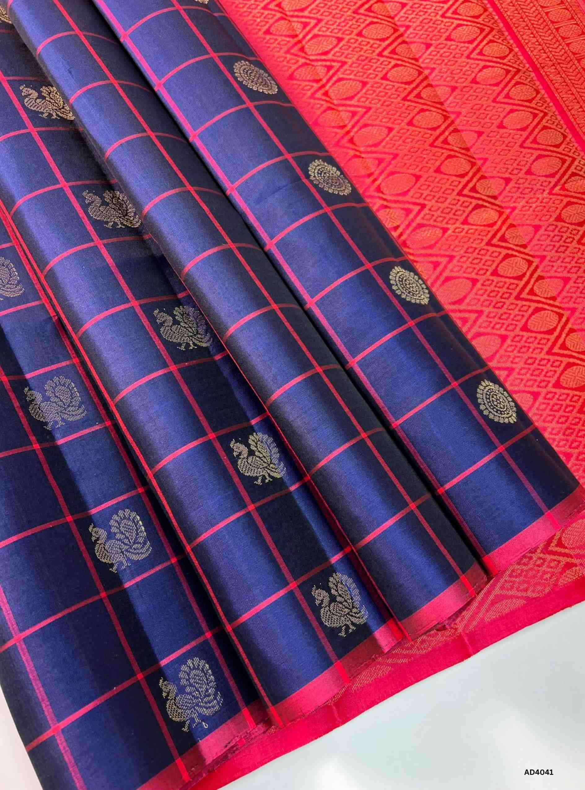 The Navy Blue & Pink Checkered Soft Silk Saree is a striking handwoven creation that radiates festive charm and cultural richness. The deep navy blue shade symbolizes elegance and prosperity, while the lively pink adds vibrancy and auspicious brilliance. The checkered weave, enhanced with delicate motifs, creates a rhythmic visual appeal, while zari highlights on the border and pallu lend a shimmering finish. Perfect for weddings, temple ceremonies, and cultural gatherings, this saree embodies South Indian