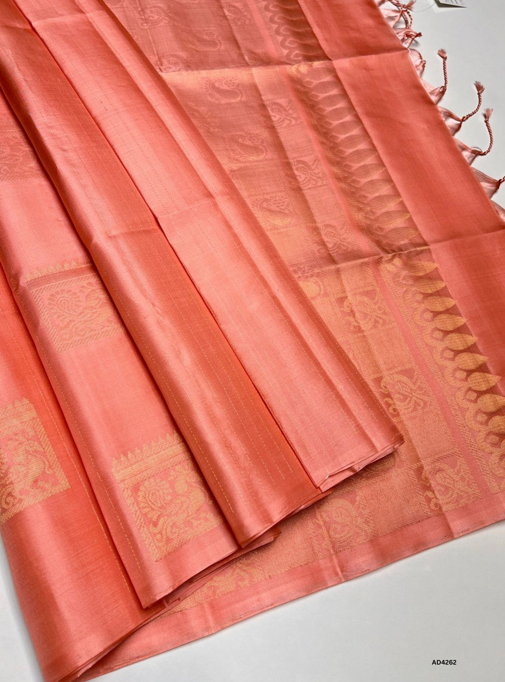 The Peach Soft Silk Saree is a graceful handwoven creation that radiates subtle elegance and cultural richness. The peach shade conveys serenity, devotion, and feminine charm, while the zari borders and lustrous drape elevate its grandeur. Its coordinated blouse completes the ensemble, making this saree perfect for weddings, temple ceremonies, and festive occasions. A timeless piece of Kanchipuram artistry, it blends pastel serenity with contemporary sophistication.