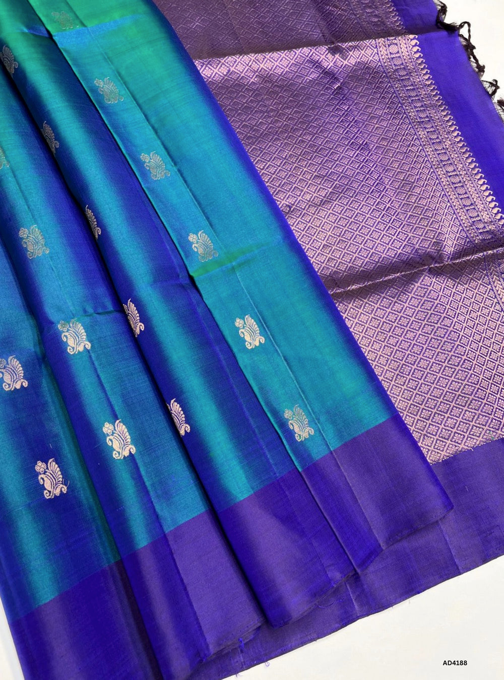 The Peacock Blue & Purple Soft Silk Saree is a majestic handwoven creation that radiates festive brilliance and cultural elegance. The peacock blue shade symbolizes prosperity, devotion, and timeless charm, while the purple conveys royalty, spirituality, and celebratory grandeur. Enhanced with pure gold zari borders and a lustrous drape, this saree is perfect for weddings, temple ceremonies, and cultural gatherings. A timeless piece of artistry, it blends jewel‑tone vibrance with the heritage of South India