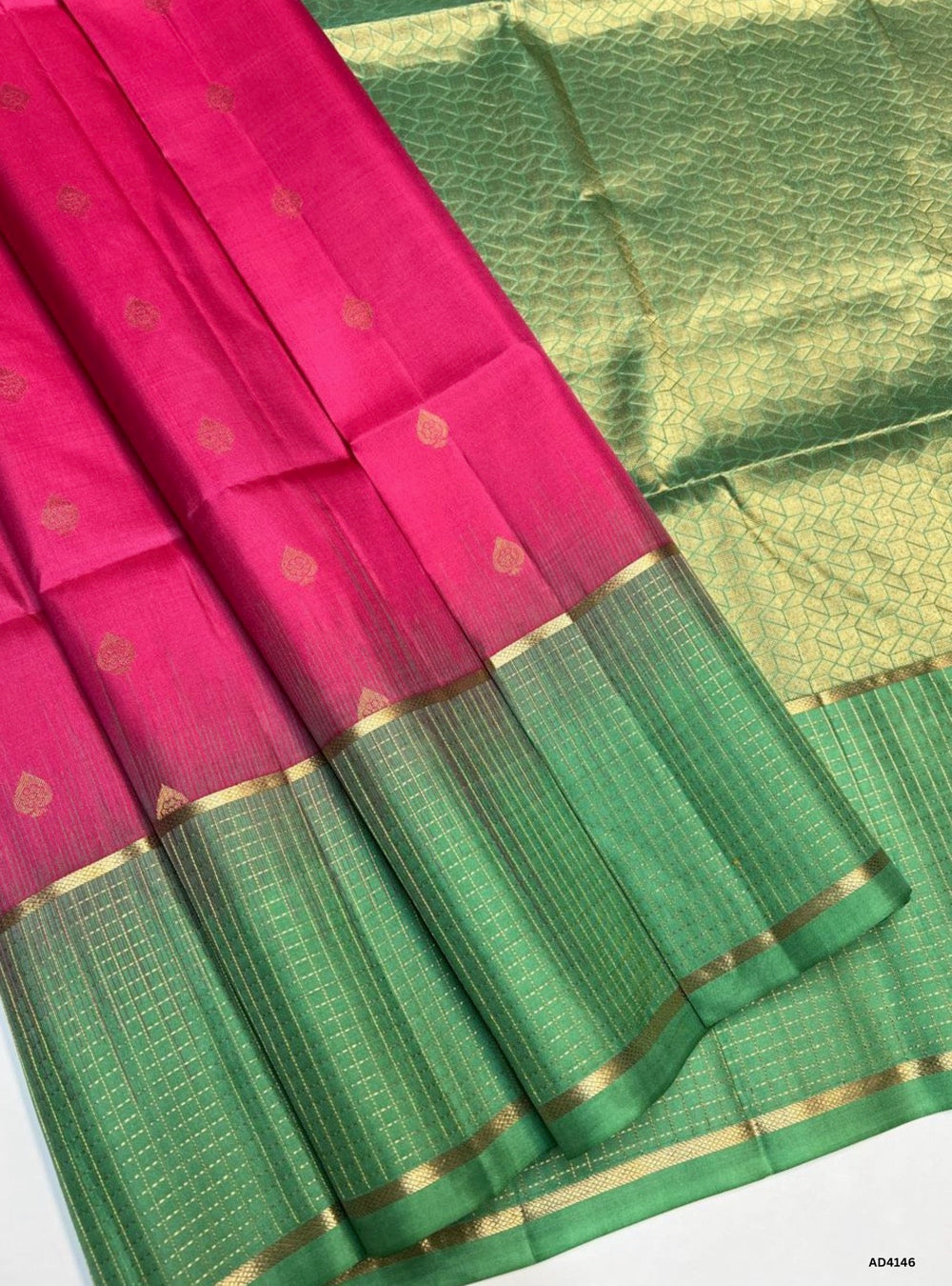 The Pink & Mint Green Checkered Retta Pet Soft Silk Saree is a lively handwoven creation that radiates festive charm and cultural elegance. The bright pink shade conveys joy, celebration, and feminine grace, while the mint green adds refreshing brightness and youthful vibrance. The checkered weave across the body enhances its visual appeal, while the Retta Pet temple‑inspired double line border enriches the saree with timeless grandeur. Enhanced with pure gold zari and a lustrous drape, this saree is perfec