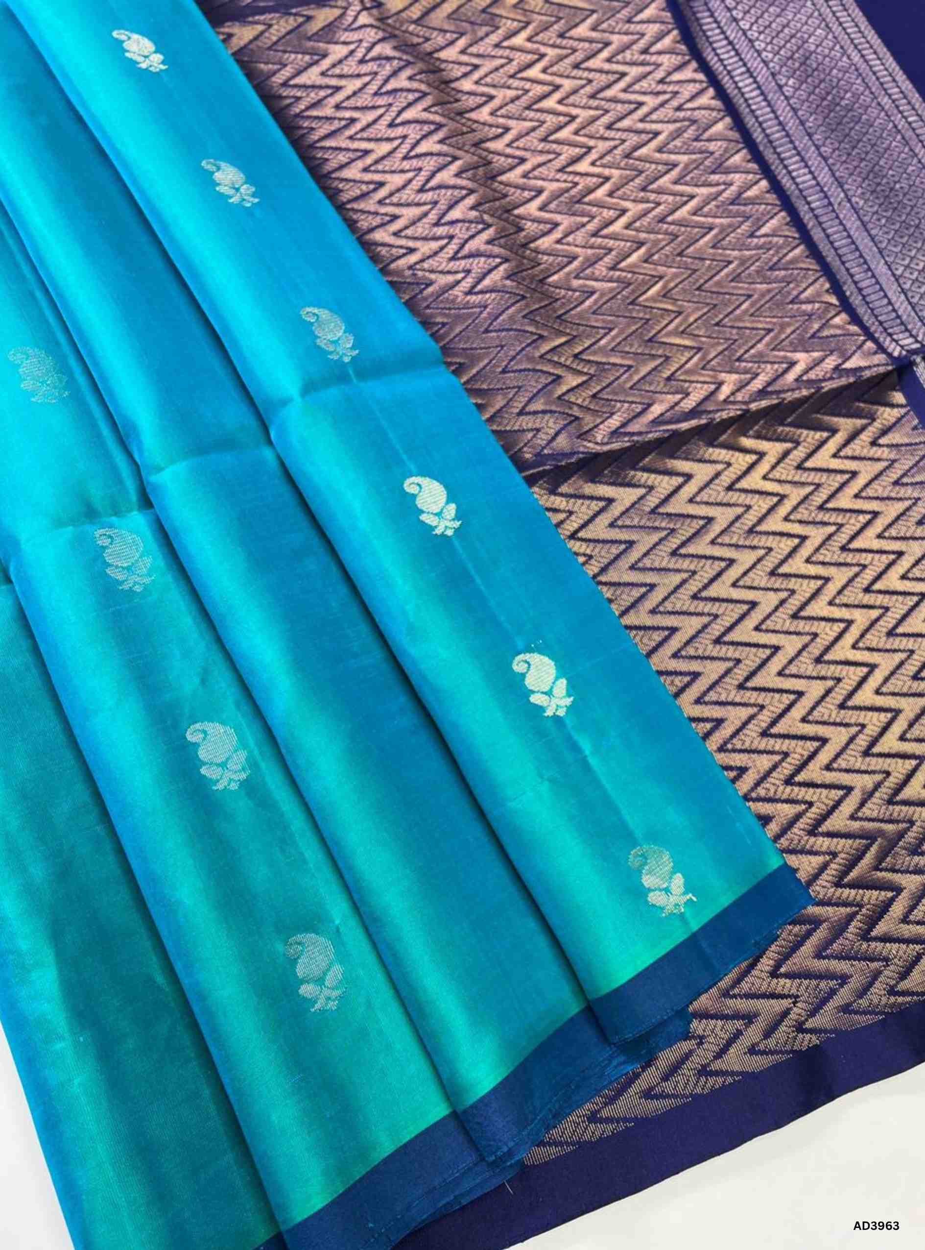 The Rama Blue & Ink Blue Bhutta Soft Silk Saree is a majestic handwoven creation that celebrates festive grandeur with a jewel‑tone palette. The refreshing rama blue shade radiates vibrancy and cultural charm, while the deep ink blue adds regal sophistication. The bhutta weave, adorned with intricate motifs, enhances the saree’s artistry, while zari highlights on the border and pallu lend a shimmering appeal. Perfect for weddings, temple ceremonies, and cultural gatherings, this saree embodies South Indian