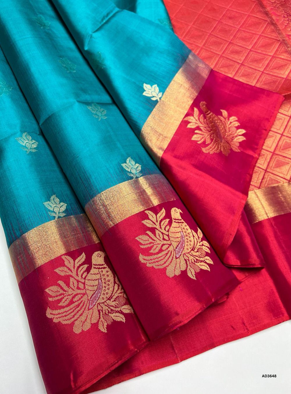 The Tiffany Blue & Reddish Pink Soft Silk Saree is a radiant handwoven creation featuring a luminous Tiffany Blue body enriched with shimmering bhutta motifs. These small, repeating zari designs add depth and texture to the fabric, enhancing its elegance and visual richness. The artistry of the bhutta weave celebrates traditional craftsmanship, while the reddish pink contrast adds vibrancy. Perfect for weddings, festive occasions, and cultural gatherings, this saree highlights motif detailing as its central
