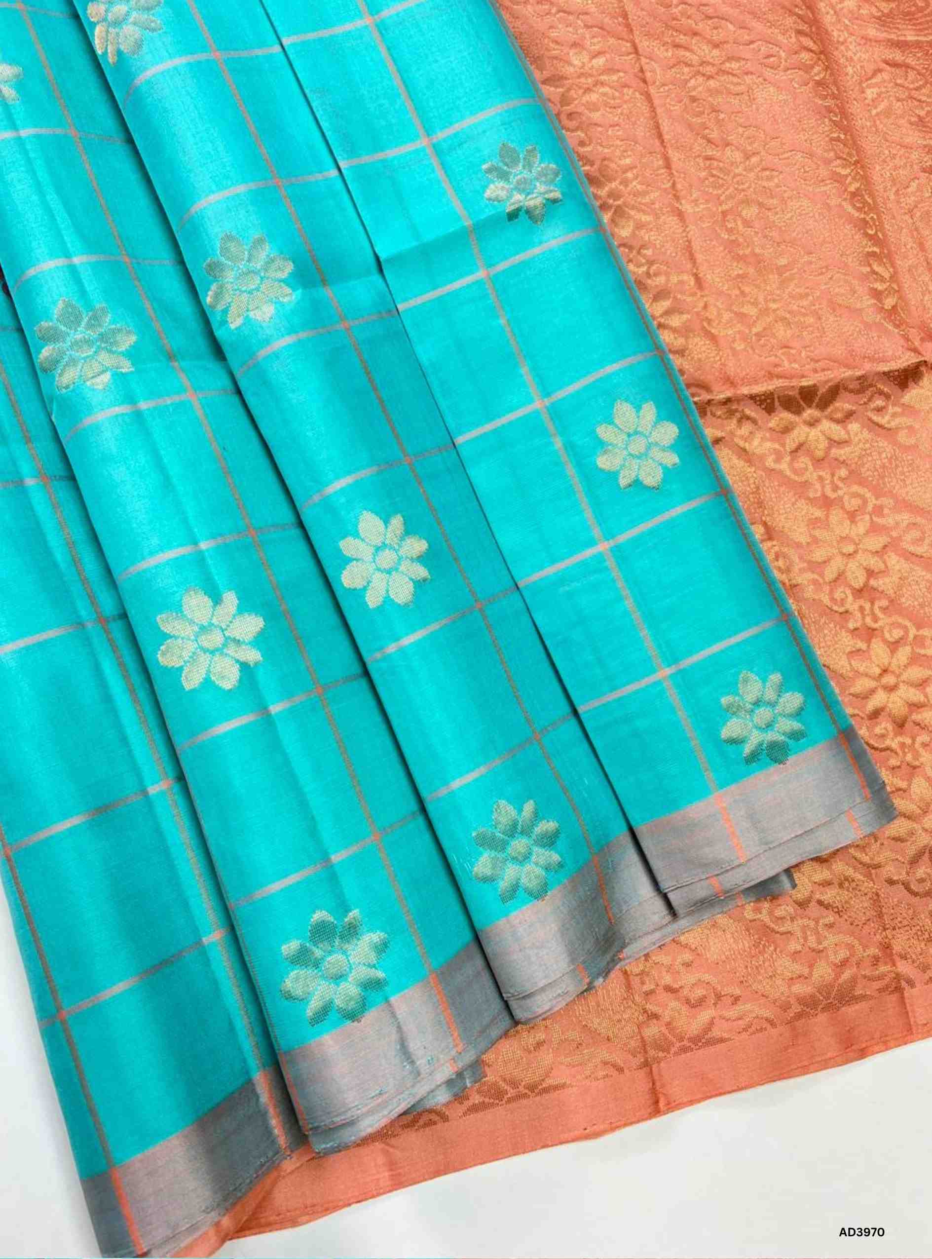 The Turquoise & Peach Checkered Bhutta Soft Silk Saree is a luminous handwoven creation that celebrates festive grandeur with a refreshing dual‑tone palette. The vibrant turquoise shade radiates modern energy and freshness, while the peach tone adds softness and celebratory warmth. The checkered bhutta weave, adorned with delicate motifs, enhances the saree’s artistry, while zari highlights on the border and pallu lend a shimmering appeal. Perfect for weddings, temple ceremonies, and cultural gatherings, th