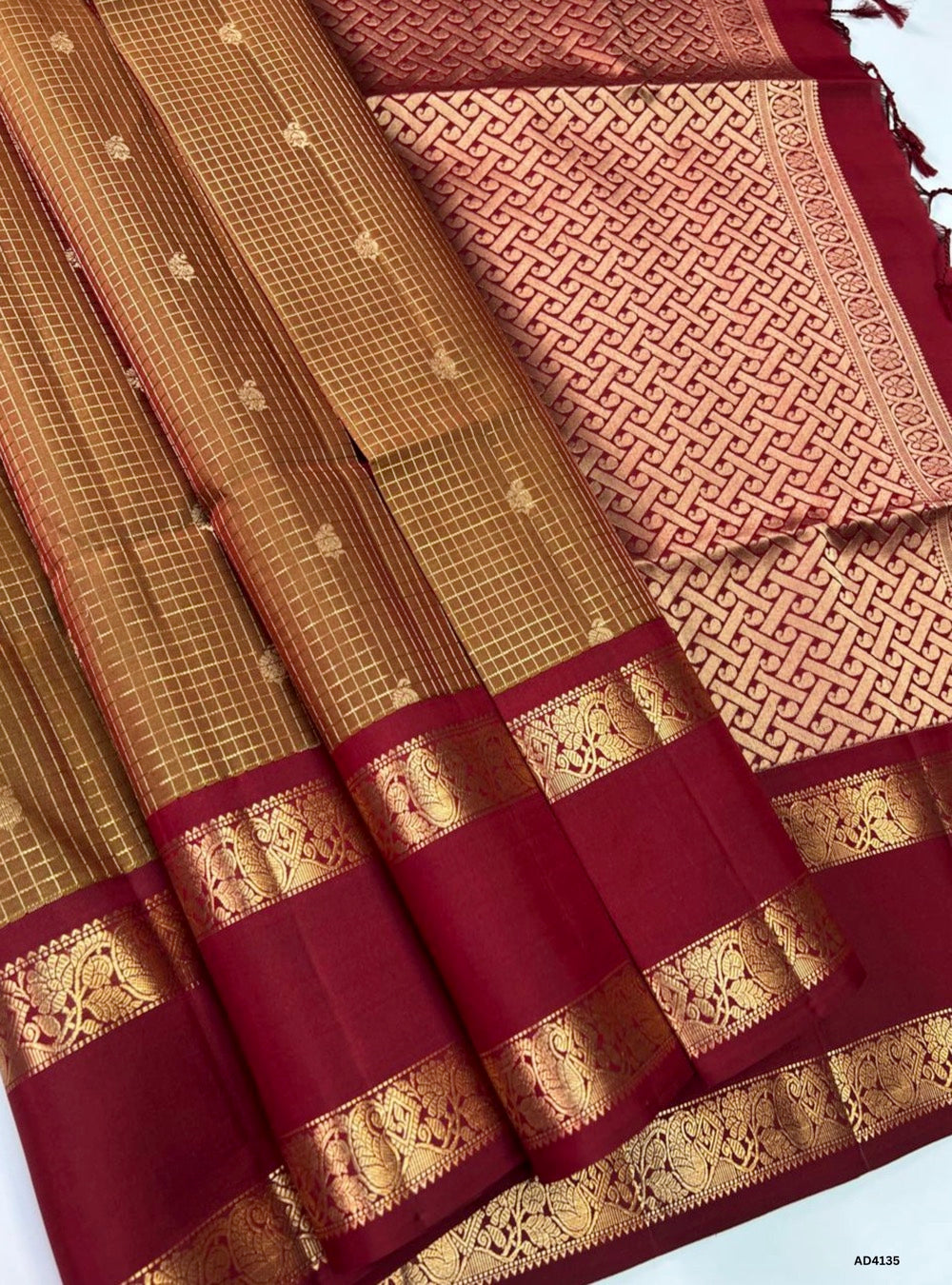 The Wooden Cream & Maroon Checkered Retta Pet Soft Silk Saree is a refined handwoven creation that radiates cultural elegance and festive grandeur. The wooden cream shade conveys subtle sophistication, calmness, and natural charm, while the maroon adds richness, devotion, and regal depth. The checkered weave across the body enhances its visual appeal, while the Retta Pet temple‑inspired double line border enriches the saree with timeless artistry. Enhanced with pure gold zari and a lustrous drape, this sare