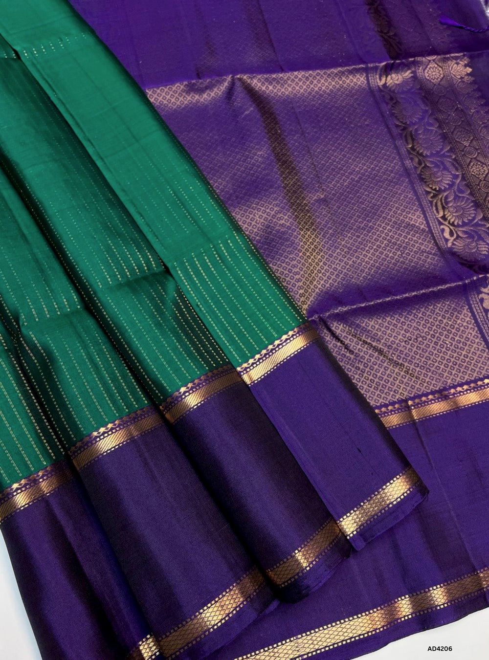 The Green & Purple Vairaoosi X Retta Pet Soft Silk Saree is a majestic handwoven creation that unites two iconic motifs of Kanchipuram weaving. The green shade conveys prosperity, freshness, and festive brilliance, while the purple adds regal depth, devotion, and timeless elegance. The body features the Vairaoosi diamond motif, symbolizing wealth and auspiciousness, while the Retta Pet double line temple border enriches the saree with heritage artistry. Enhanced with pure gold zari and a lustrous drape, thi