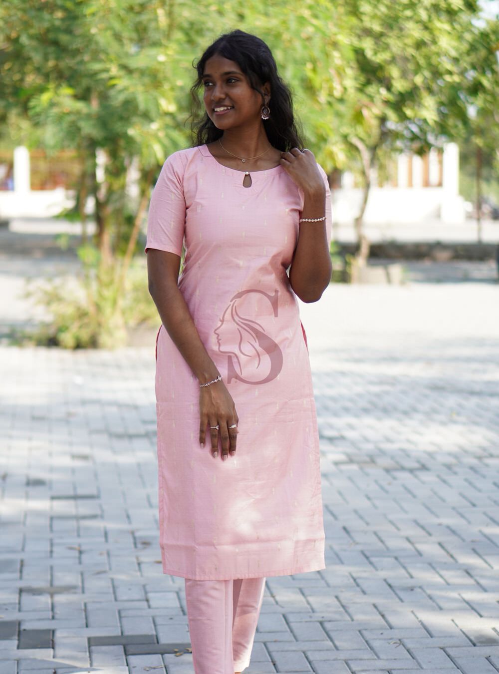 Woman wearing a pink traditional outfit with a decorative design outdoors.