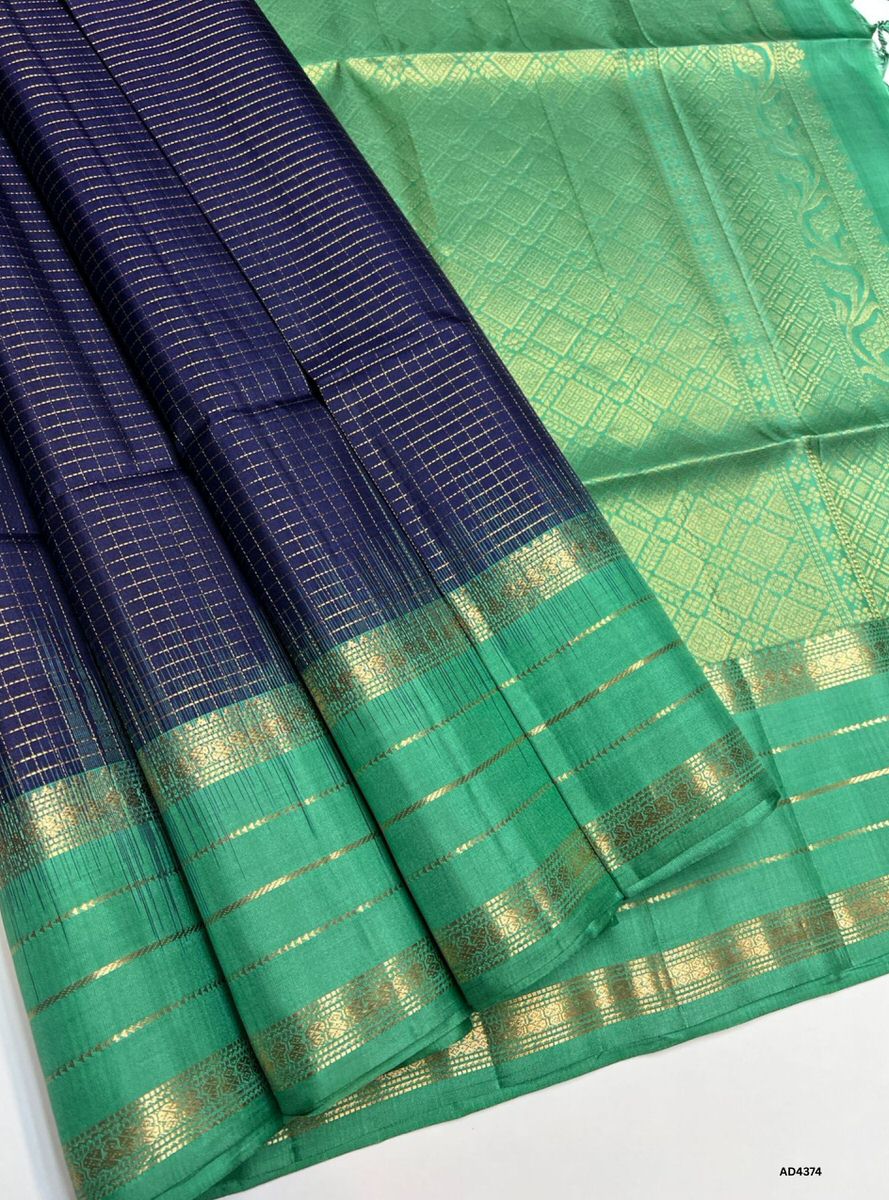 The Navy Blue & Mint Green Checkered Retta Pet Soft Silk Saree is a graceful handwoven creation that radiates cultural richness and festive charm. The navy blue shade conveys devotion, sophistication, and timeless elegance, while the mint green checks add freshness, vibrance, and celebratory brilliance. Enhanced with pure gold zari borders and a lustrous drape, this saree is perfect for weddings, temple ceremonies, and festive occasions. A timeless masterpiece, it blends regal depth with pastel vibrance in 