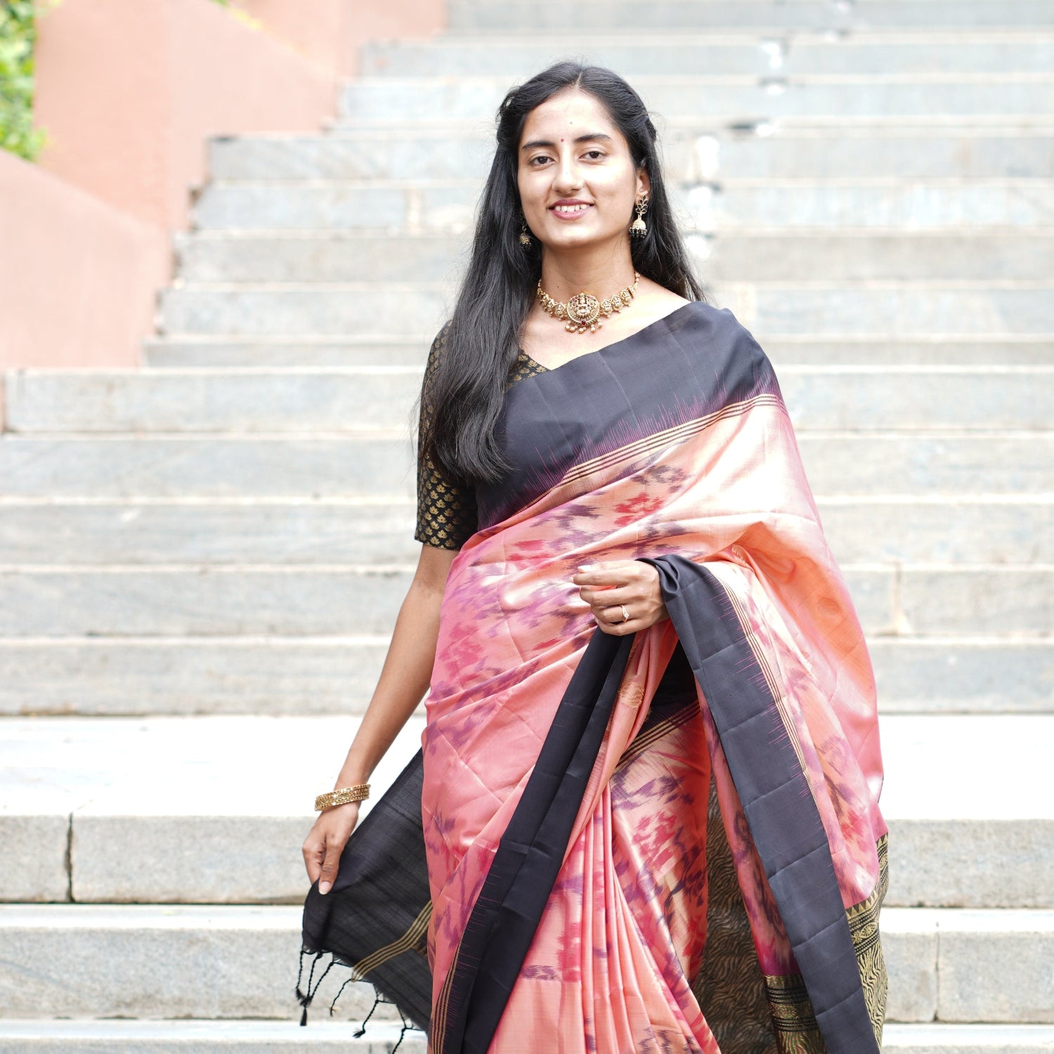 Woman wearing a black and pink saree standing on steps outdoors