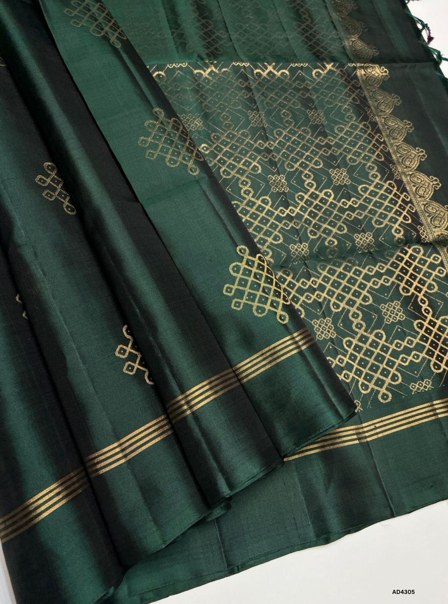 The Dark Green Kolam Soft Silk Saree is a majestic handwoven creation that radiates auspicious charm and cultural richness. The deep green shade symbolizes prosperity, devotion, and timeless elegance, while the Kolam‑inspired Kanchipuram border enriched with pure gold zari elevates its grandeur. Its lustrous drape and coordinated blouse complete the ensemble, making this saree perfect for weddings, temple ceremonies, and festive occasions. A true testament to Kanchipuram artistry, it blends heritage Kolam m