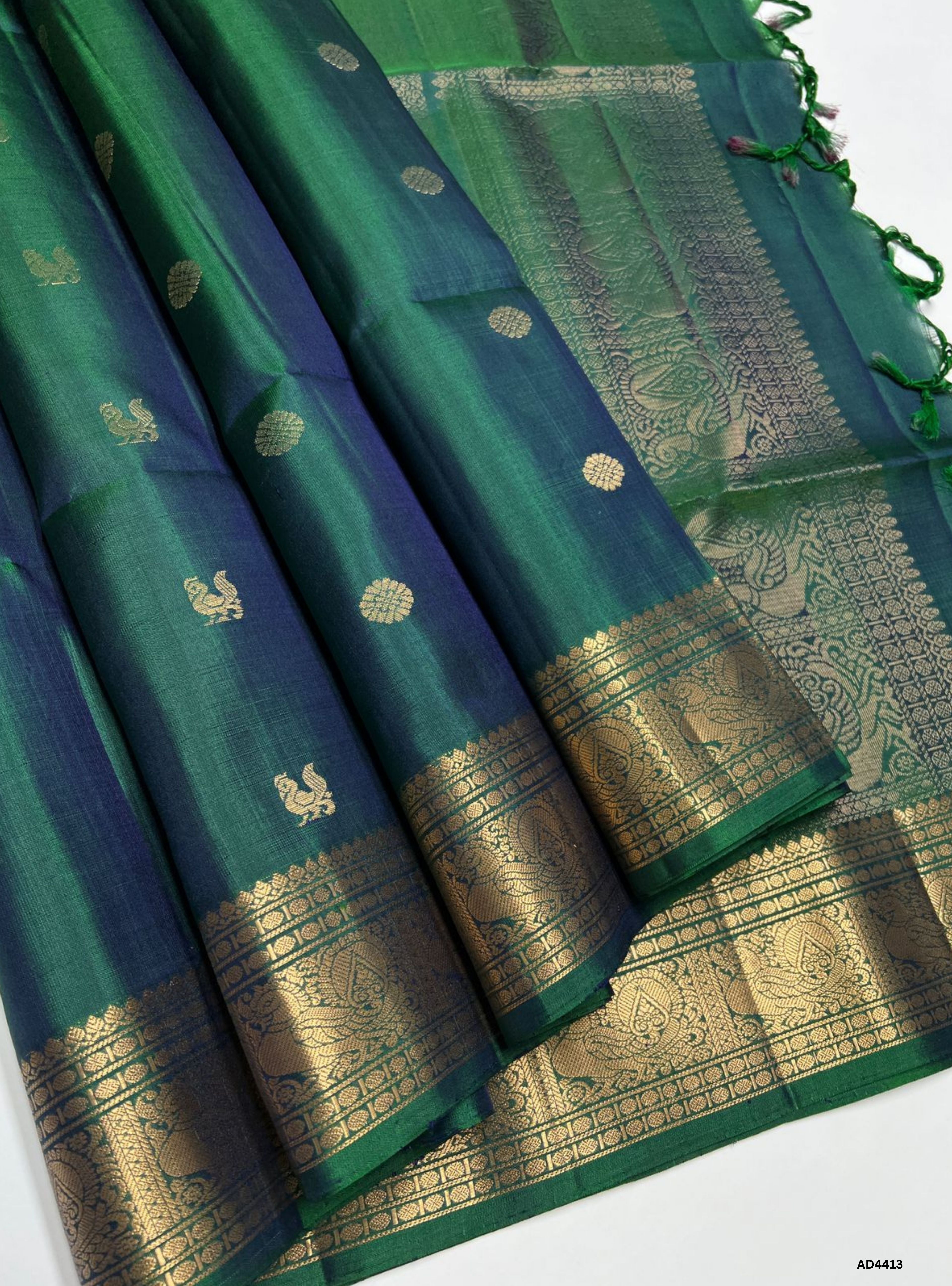 The Dual Tone Green Kanchi Border Soft Silk Saree with Half Fine Tested Gold Zari is a handwoven masterpiece that unites lush green vibrance with heritage temple borders, making it ideal for weddings, festive occasions, and cultural ceremonies.