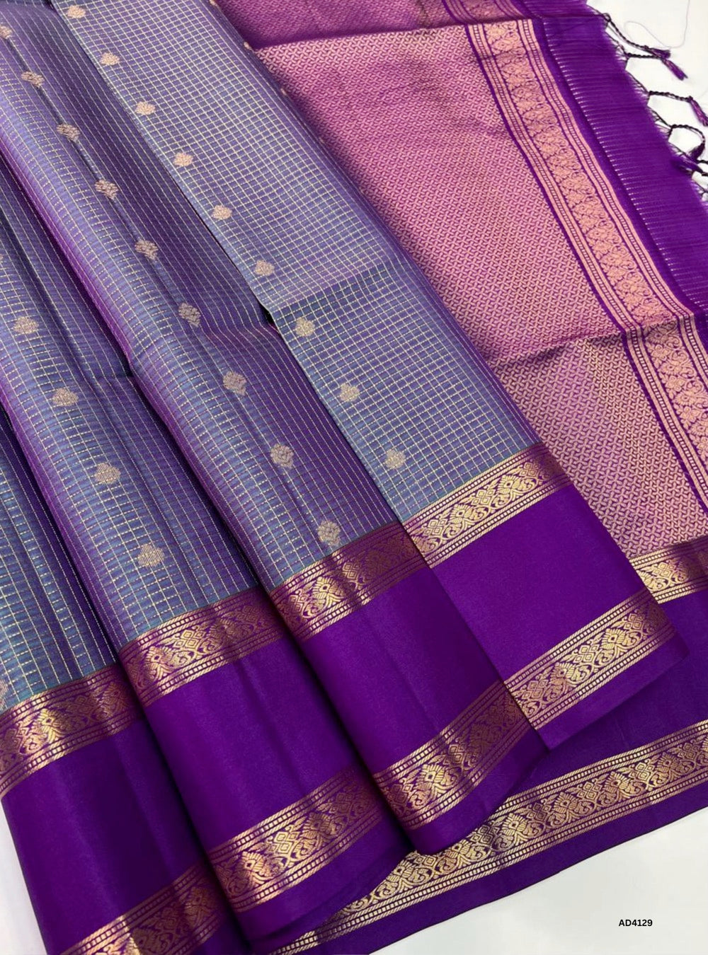 The Dual Tone Purple & Purple Checkered Retta Pet Soft Silk Saree is a majestic handwoven creation that radiates regal charm and cultural richness. The interplay of lighter and deeper purple shades conveys devotion, elegance, and timeless sophistication. The checkered weave across the body enhances its visual appeal, while the Retta Pet temple‑inspired double line border enriches the saree with heritage artistry. Enhanced with pure gold zari and a lustrous drape, this saree is perfect for weddings, temple c
