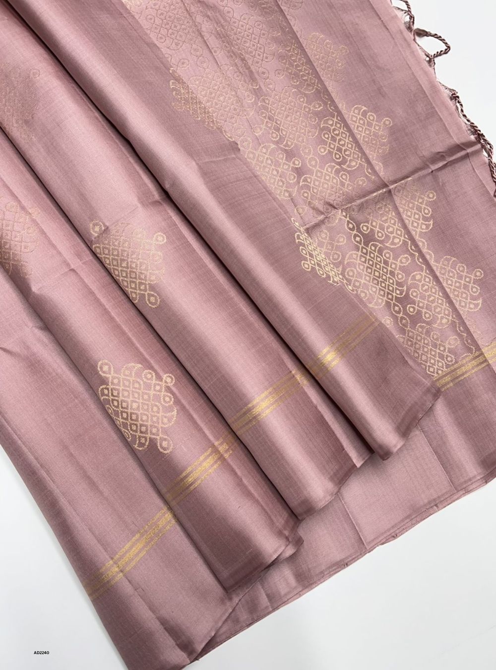 Folded mauve saree with gold patterns on a white background