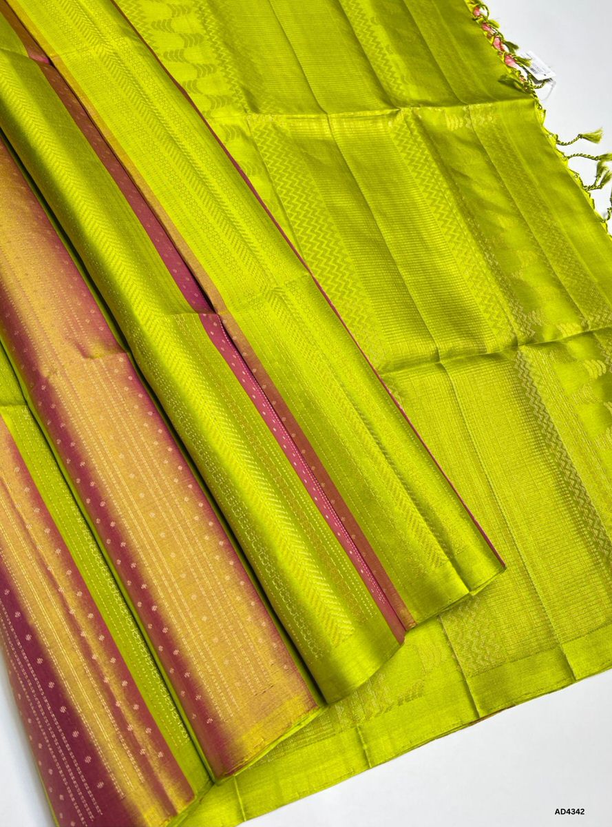 The Gold & Parrot Green Soft Silk Saree is a luminous handwoven creation that radiates festive grandeur and cultural richness. The golden body symbolizes prosperity, auspiciousness, and timeless elegance, while the parrot green contrast conveys freshness, vibrance, and celebratory charm. Enhanced with pure gold zari borders and a lustrous drape, this saree is perfect for weddings, temple ceremonies, and festive occasions. A timeless masterpiece, it blends regal brilliance with nature‑inspired vibrance in So