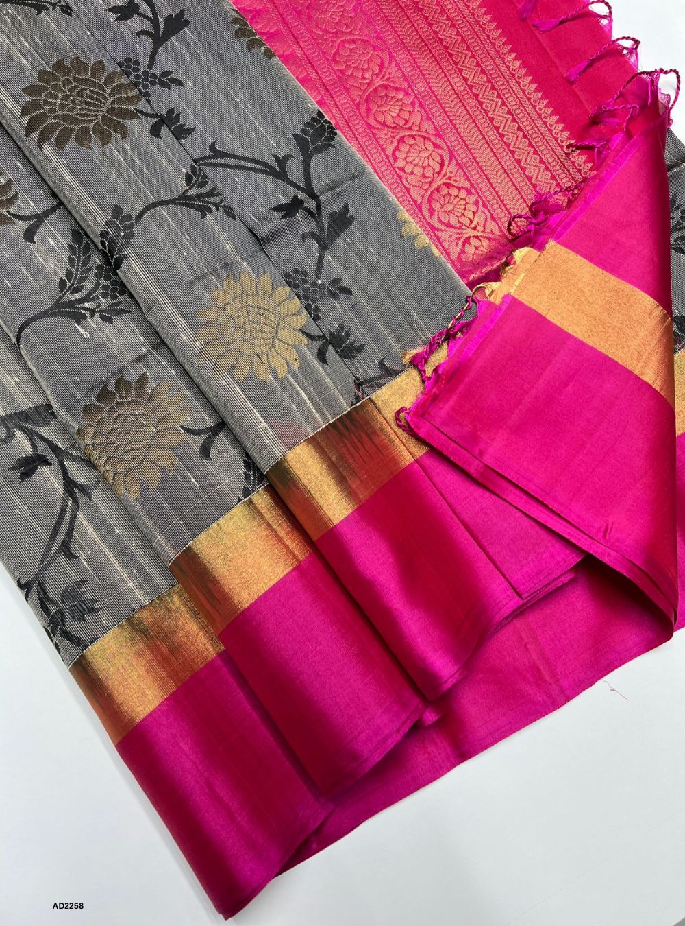 Gray saree with floral patterns and pink border on a white background