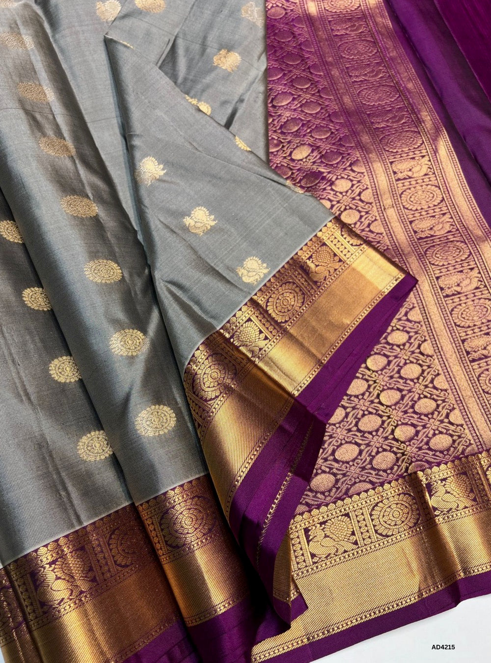 The Grey & Magenta Kanchi Border Soft Silk Saree is a striking handwoven creation that radiates cultural grandeur and festive brilliance. The grey shade conveys sophistication, balance, and timeless elegance, while the magenta adds vibrance, devotion, and celebratory warmth. The traditional Kanchi border enriched with pure gold zari elevates its heritage appeal, while the lustrous drape and coordinated blouse complete the ensemble. Perfect for weddings, temple ceremonies, and festive occasions, this saree e
