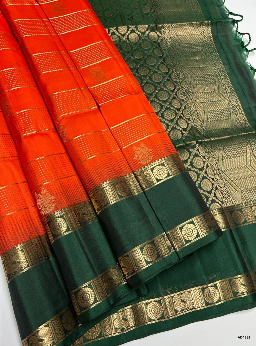 The Orange & Green Checkered Retta Pet Soft Silk Saree is a radiant handwoven creation that embodies festive charm and cultural grandeur. The orange shade conveys joy, devotion, and celebratory vibrance, while the green checks symbolize prosperity, auspiciousness, and timeless tradition. Enhanced with pure gold zari borders and a lustrous drape, this saree is perfect for weddings, temple ceremonies, and festive occasions. A timeless masterpiece, it blends vibrant dual tones with the heritage Retta Pet check