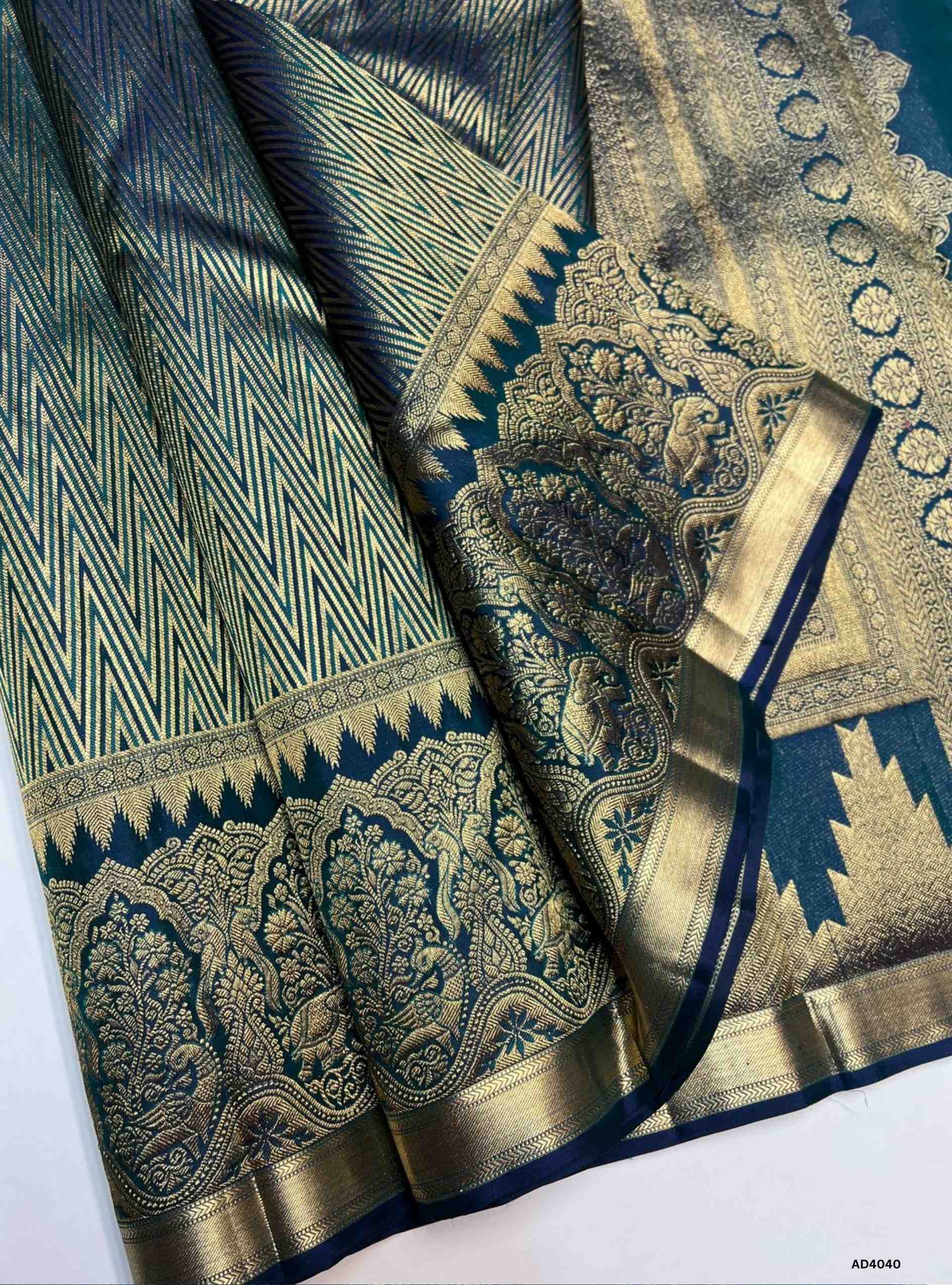 The Peacock Blue Kanjeevaram Bridal Soft Silk Saree is a majestic handwoven creation designed for weddings and grand occasions. The regal peacock blue shade symbolizes prosperity, joy, and auspicious brilliance, making it a timeless bridal choice. Its lustrous drape is enriched with heavy gold zari, temple‑inspired borders, and a grand pallu featuring traditional motifs of peacocks, lotuses, and geometric artistry. This saree embodies the heritage of Kanchipuram weaving, combining elegance with cultural gra