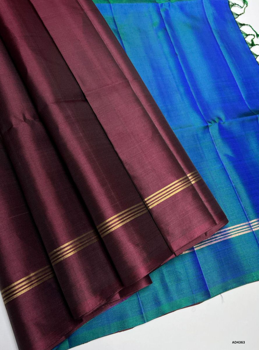 The Peacock Blue & Maroon Plain Soft Silk Saree is a graceful handwoven creation that radiates elegance and cultural richness. The peacock blue shade symbolizes prosperity, devotion, and timeless vibrance, while the maroon contrast conveys heritage depth, regal charm, and festive grandeur. Enhanced with pure gold zari borders and a lustrous drape, this saree is perfect for weddings, temple ceremonies, and celebratory occasions. A versatile masterpiece, it blends jewel‑tone brilliance with plain weave artist
