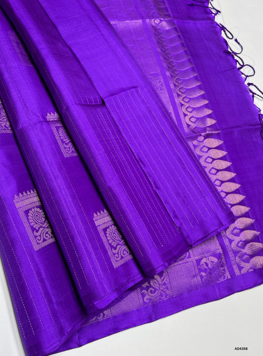 The Purple Plain Soft Silk Saree is a graceful handwoven creation that radiates regal charm and cultural richness. The single‑tone purple shade symbolizes devotion, sophistication, and timeless elegance. Its plain body highlights the lustrous drape of premium soft silk, while the zari border and pallu add heritage artistry. Enhanced with pure gold zari detailing, this saree is perfect for weddings, temple ceremonies, and festive occasions, embodying the grandeur of Kanchipuram weaving in its purest form.