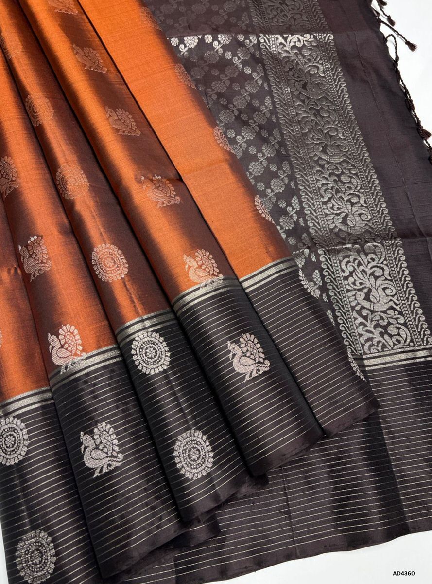The Rust & Coffee Brown Bhutta Soft Silk Saree is a radiant handwoven creation that celebrates festive charm and cultural grandeur. The rust shade conveys warmth, devotion, and auspicious brilliance, while the coffee brown contrast adds earthy sophistication and heritage depth. The bhutta motifs scattered across the body enrich the saree with ornamental artistry. Enhanced with pure gold zari borders and a lustrous drape, this saree is perfect for weddings, temple ceremonies, and celebratory occasions. A tim