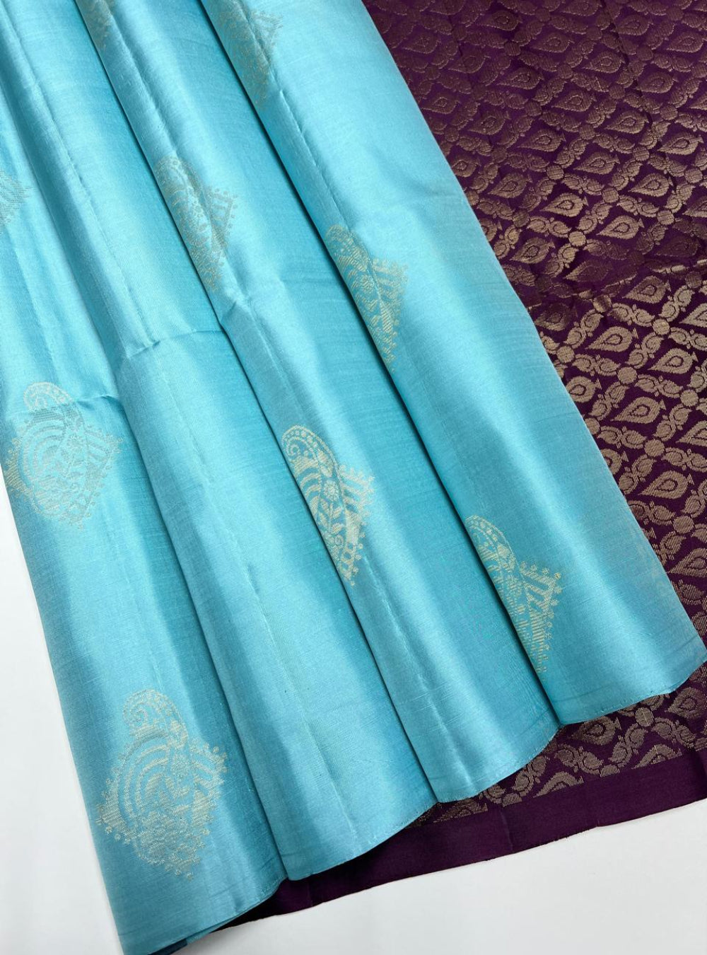 The Sky Blue & Plum Soft Silk Saree is a refreshing handwoven creation featuring a luminous sky blue body enriched with shimmering zari. Its regal plum border and pallu highlight the intricate bhutta weave motifs, adding elegance and traditional charm. Perfect for weddings, festive occasions, and cultural gatherings, this saree blends soothing brilliance with timeless bhutta craftsmanship.