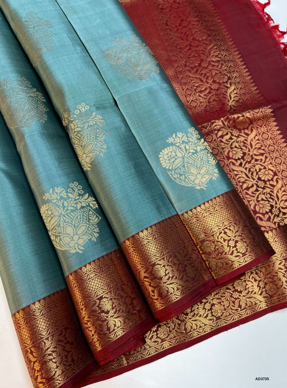 The Teal & Maroon Soft Silk Saree is a striking handwoven creation featuring a luminous teal body enriched with the traditional Bhutta motifs. Its highlight is the Jacquard woven maroon border, which adds depth, texture, and grandeur to the saree. The interplay of teal and maroon creates a bold yet elegant contrast, making this saree ideal for weddings, festive occasions, and cultural gatherings. It beautifully showcases South Indian weaving heritage with a refined modern appeal