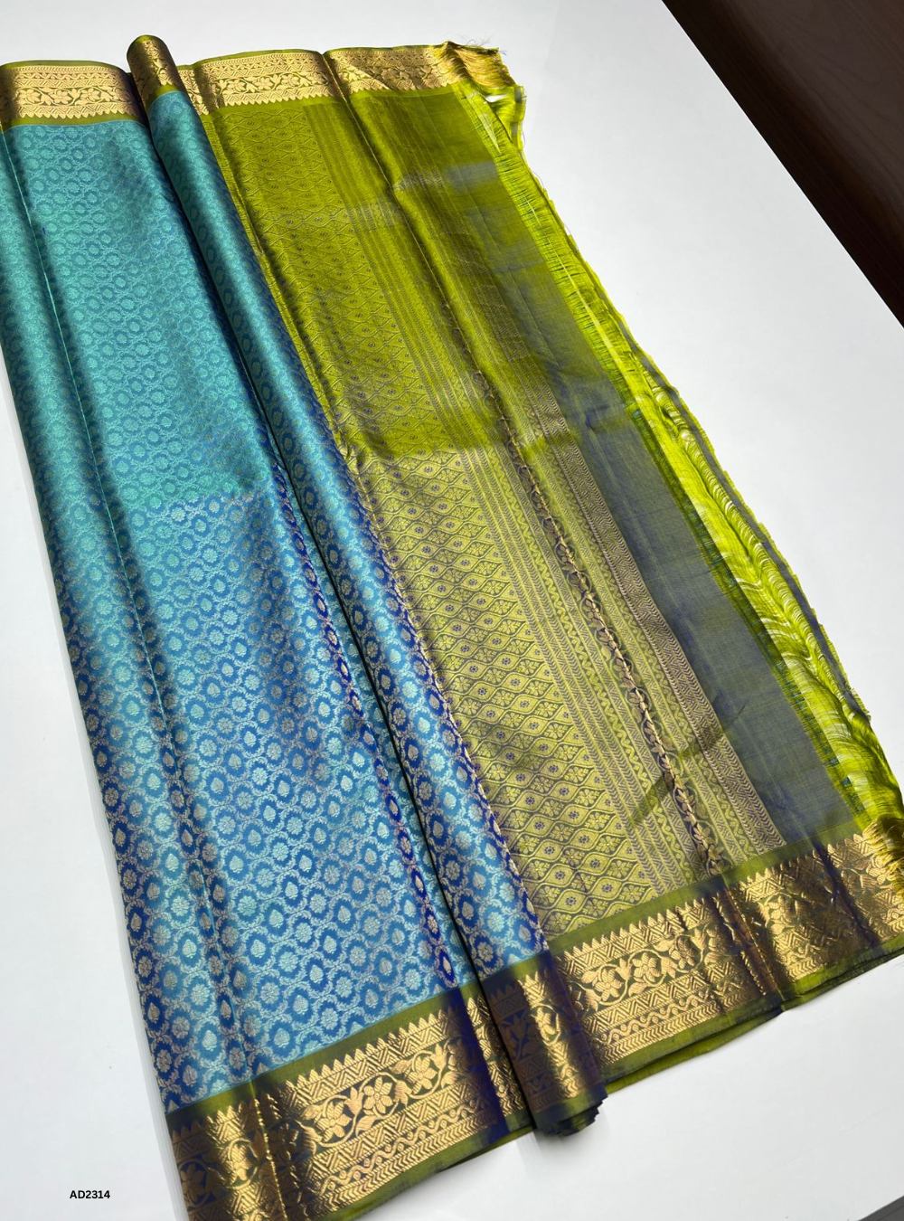 Two traditional sarees, one blue and one green with gold borders, on a white surface.