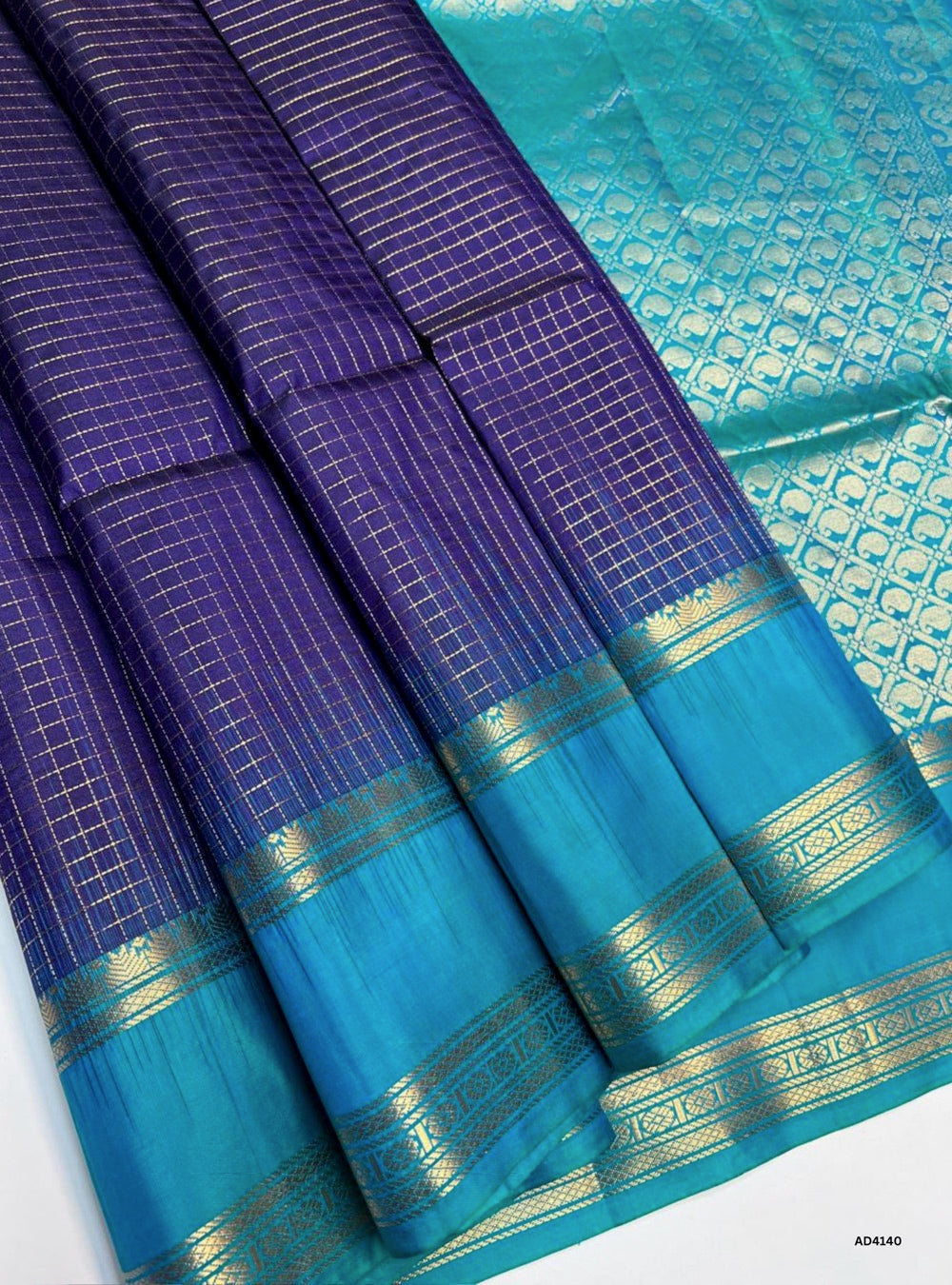 
The Violet & Rama Green Checkered Retta Pet Soft Silk Saree is a striking handwoven creation that radiates festive grandeur and cultural richness. The violet shade conveys devotion, elegance, and regal charm, while the rama green adds celebratory brilliance and youthful vibrance. The checkered weave across the body enhances its visual appeal, while the Retta Pet temple‑inspired double line border enriches the saree with timeless artistry. Enhanced with pure gold zari and a lustrous drape, this saree is per
