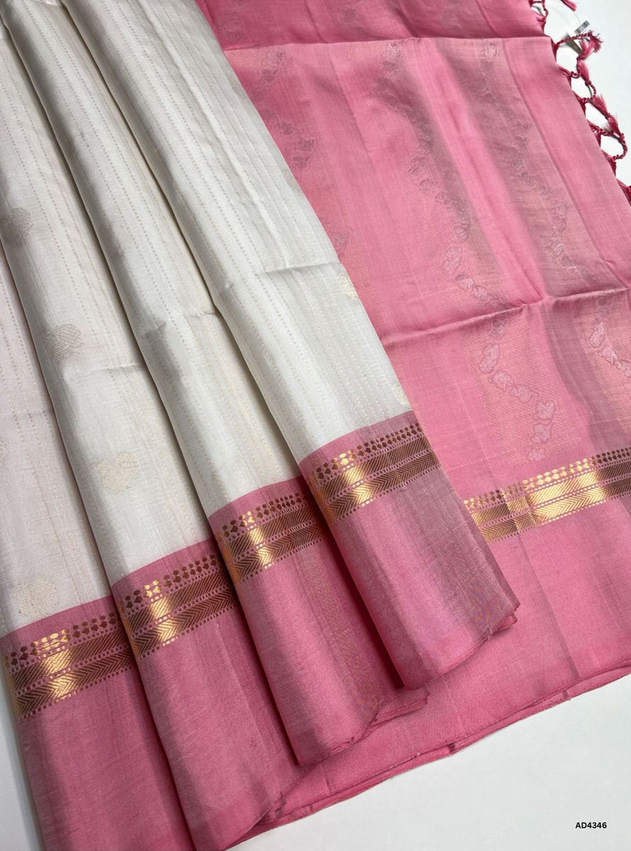 The White & Pink Vairoosi X Kanchi Border Soft Silk Saree is a luminous handwoven creation that unites the serenity of white with the festive charm of pink. The body features the Vairoosi diamond motif, symbolizing prosperity and auspiciousness, while the temple‑inspired Kanchi border enriches the saree with timeless heritage. The pink shade conveys joy, devotion, and feminine elegance, while the white radiates purity and grace. Enhanced with pure gold zari and a lustrous drape, this saree is perfect for we